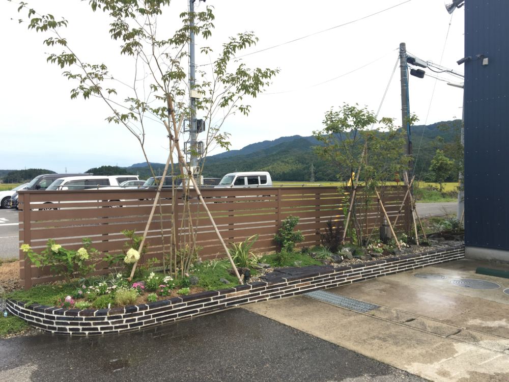 風除けも兼ねた目隠しフェンスが植栽を引き立てます。
陶板レンガを積んだ花壇にアオダモ、ジューンベリー、ツリバナ、ノリウツギなどの落葉樹をメインに植栽。
冬は落葉するので風雪の抵抗が低減します。
足元はタイムやヤブラン、初雪カズラといった多年草を。
入り口側は一年草のスペースで、季節の花々を楽しめます。

