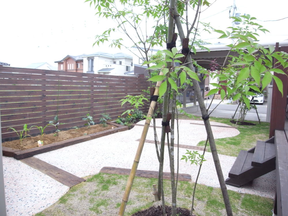 デッキからの眺め。
枕木で土留めをした家庭菜園のスペースで収穫した野菜を運ぶ動線は、瓦チップのアプローチがテラスと室内を繋いでいます。
中庭部分は、枕木のステップからレンガチップの洗い出しでテラスを設け、気になっていた雑草の悩みを解決しました。
既存のウッドデッキの下部にも防草シートを布設してあります。