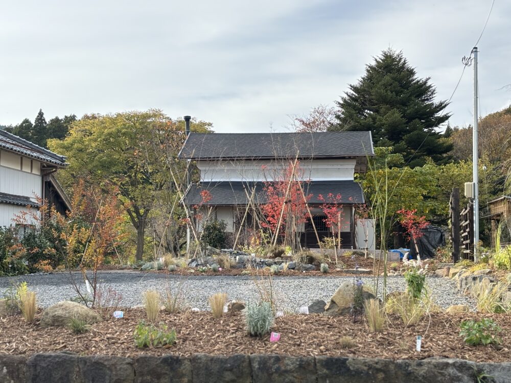 手前の既存の石積み花壇には自然の景色に馴染むオーナメンタルグラスや宿根草を植栽。ラベンダーやネペタなど草丈の高い草花が風のそよぎを感じさせてくれます。
奥の高さのある石積みスペースにもオーナメンタルグラスを植栽。敷地全体に一体感や奥行きが出るだけでなく、直線や曲線美の優雅さとノスタルジックな風景を創り出します。
手前の花壇と奥のお庭の間にあるスペースは既存の砂利敷駐車場。