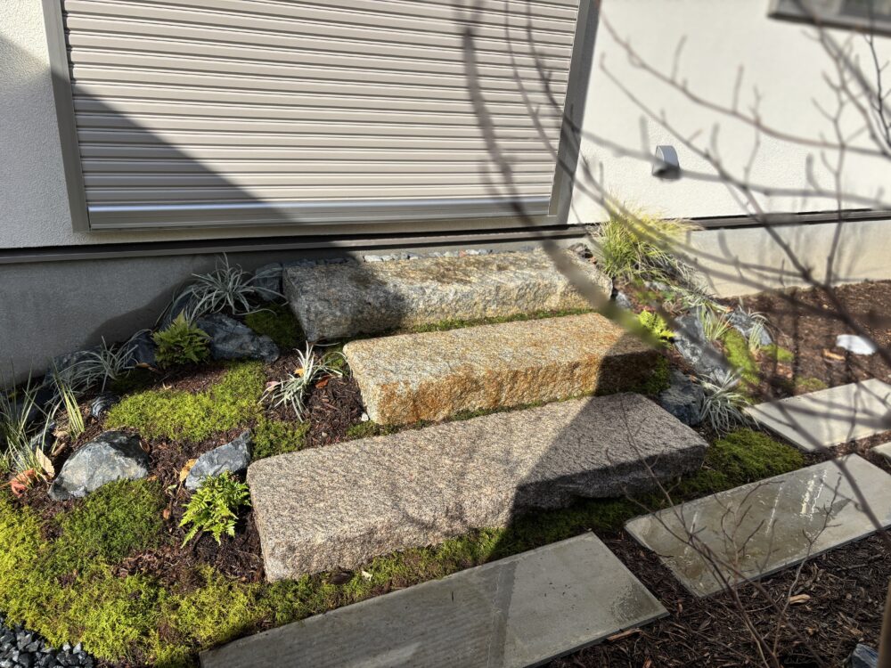 御影石の沓脱に腰を下ろすと、視線は自然と庭へ向かいます。木々の葉が風に揺れ、苔は柔らかな緑の絨毯のように広がります。冬の低い日差しが枝の影を長く伸ばし、直線的なコンクリート柵板の無機質さと苔庭の野趣が、現代的な趣を際立たせます。