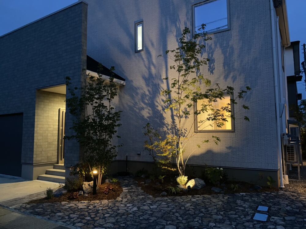 日中の爽やかな表情から一転、夜になるとお庭全体がドラマチックな光と影の世界へと表情を変えます。
玄関前のファサードエリアでは、下からライトアップされたシンボルツリーの美しい影が外壁に大きく描き出され、まるでアートのような幻想的な佇まいに。
